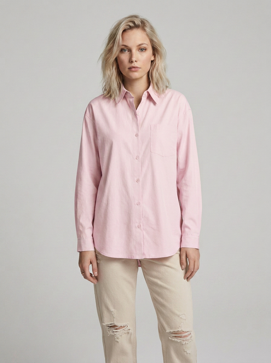 A woman modeling a light pink long-sleeve button-up shirt with beige ripped jeans against a solid light gray studio background.