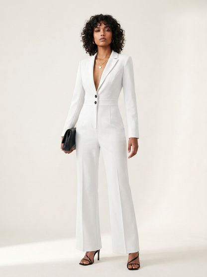 A model wearing a white tailored jumpsuit with wide legs, structured shoulders, and a deep V-neckline with three front buttons. She is holding a small black clutch and wearing black strappy heels against a clean, light beige studio background.