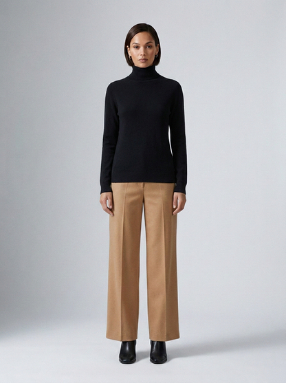 A model stands against a light gray studio background wearing a black long-sleeve turtleneck sweater and beige wide-leg trousers with black ankle boots.