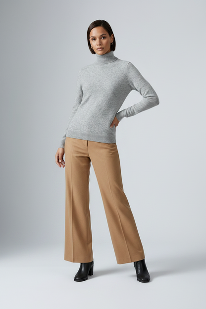 A model wearing a light gray ribbed turtleneck sweater and camel wide-leg trousers, paired with black ankle boots, against a light gray studio background.