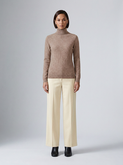 A model stands against a light gray studio background wearing a taupe-brown knit mock-neck sweater, cream wide-leg trousers, and black ankle boots.