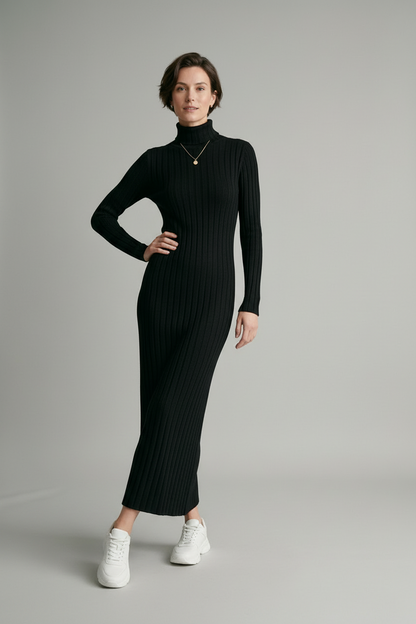 A woman modeling a long-sleeved, black ribbed turtleneck maxi dress with white sneakers, standing against a neutral light gray studio background.