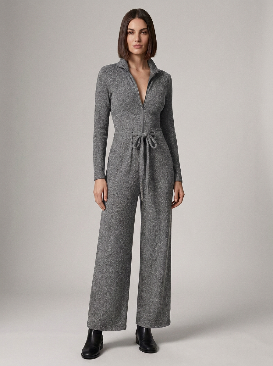 A woman modeling a gray knit jumpsuit with a half-zip collar, long sleeves, wide legs, and a drawstring waist, photographed against a plain light gray studio background.