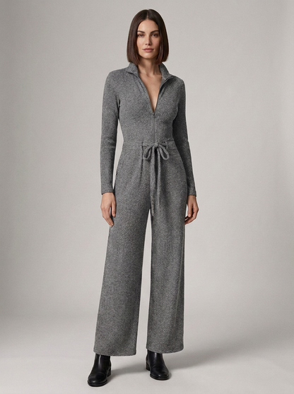 A woman modeling a gray knit jumpsuit with a half-zip collar, long sleeves, wide legs, and a drawstring waist, photographed against a plain light gray studio background.