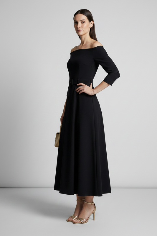 A woman models an off-the-shoulder black midi dress with three-quarter sleeves and a matching belt. She is holding a small metallic gold handbag and wearing gold strappy heels, set against a neutral light gray studio background.