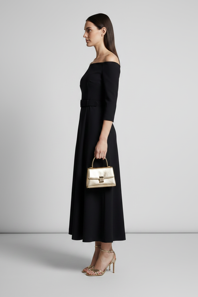 A woman models an off-the-shoulder black midi dress with three-quarter sleeves and a matching belt. She is holding a small metallic gold handbag and wearing gold strappy heels, set against a neutral light gray studio background.