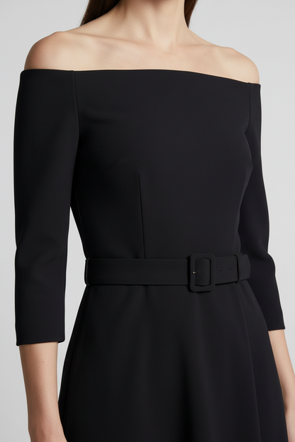 A woman models an off-the-shoulder black midi dress with three-quarter sleeves and a matching belt. She is holding a small metallic gold handbag and wearing gold strappy heels, set against a neutral light gray studio background.