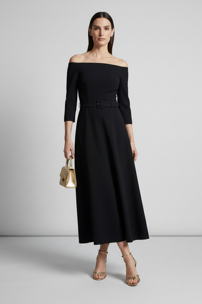 A woman models an off-the-shoulder black midi dress with three-quarter sleeves and a matching belt. She is holding a small metallic gold handbag and wearing gold strappy heels, set against a neutral light gray studio background.