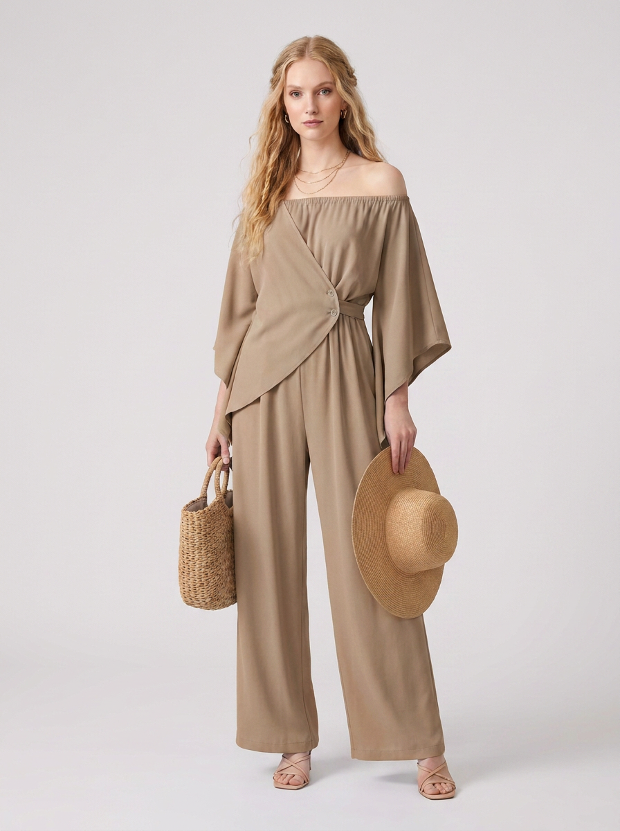 A woman models an off-the-shoulder, wide-leg jumpsuit in a warm taupe-beige color. She is holding a woven straw hat and a small woven straw tote bag against a clean, light gray studio background.