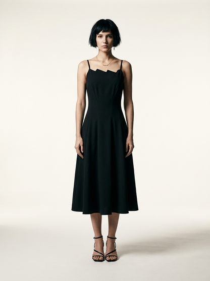 A model with a short dark bob hairstyle wearing a black midi-length spaghetti strap dress with a unique scalloped neckline, paired with black strappy high-heeled sandals, standing against a warm off-white studio background.