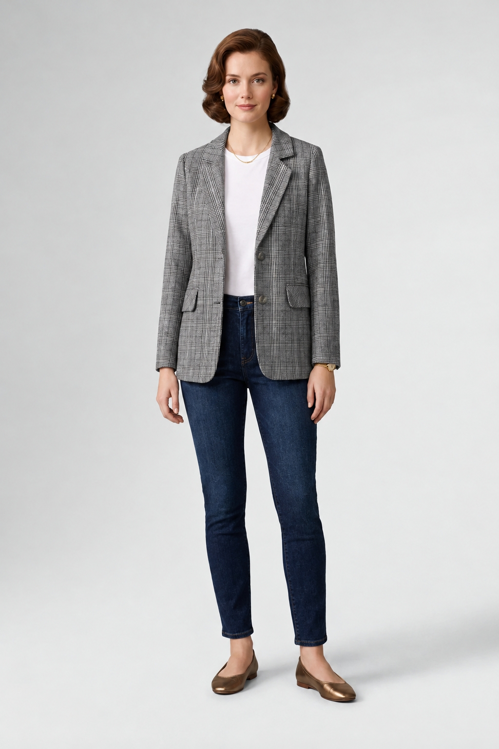 A woman modeling a gray and black checkered blazer over a white top and dark blue skinny jeans, paired with brown loafers, on a light gray studio background.
