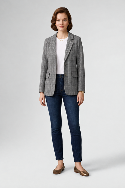 A woman modeling a gray and black checkered blazer over a white top and dark blue skinny jeans, paired with brown loafers, on a light gray studio background.