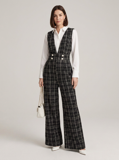 A model stands against a light gray studio background wearing a black and white plaid wide-leg vest and matching trousers over a white button-up shirt, holding a small white handbag.