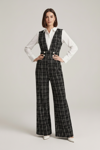 A model stands against a light gray studio background wearing a black and white plaid wide-leg vest and matching trousers over a white button-up shirt, holding a small white handbag.
