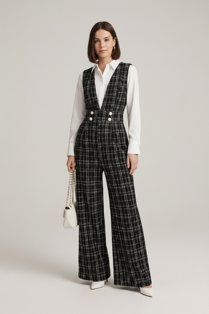 A model stands against a light gray studio background wearing a black and white plaid wide-leg vest and matching trousers over a white button-up shirt, holding a small white handbag.