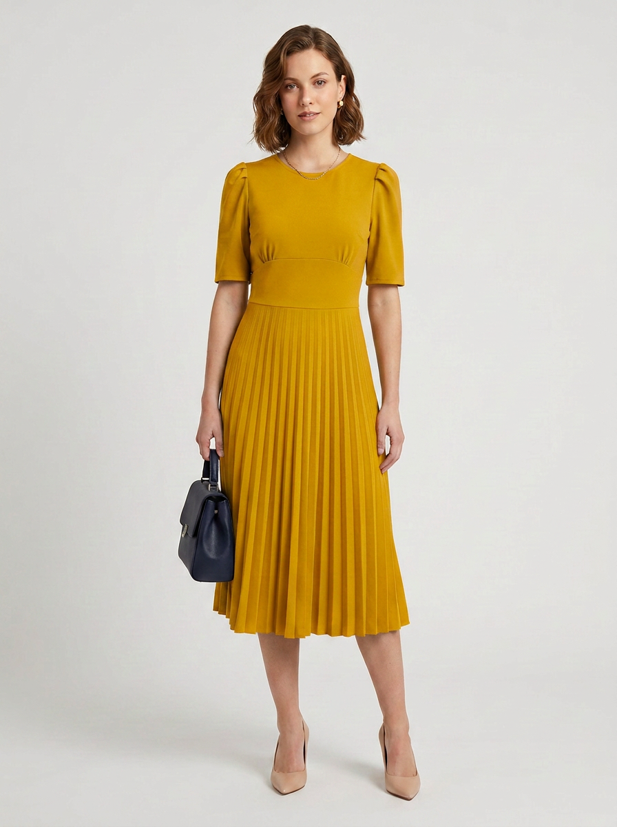 A woman modeling a mustard yellow midi dress with short puff sleeves and a pleated skirt, holding a small dark blue handbag against a light gray studio background.