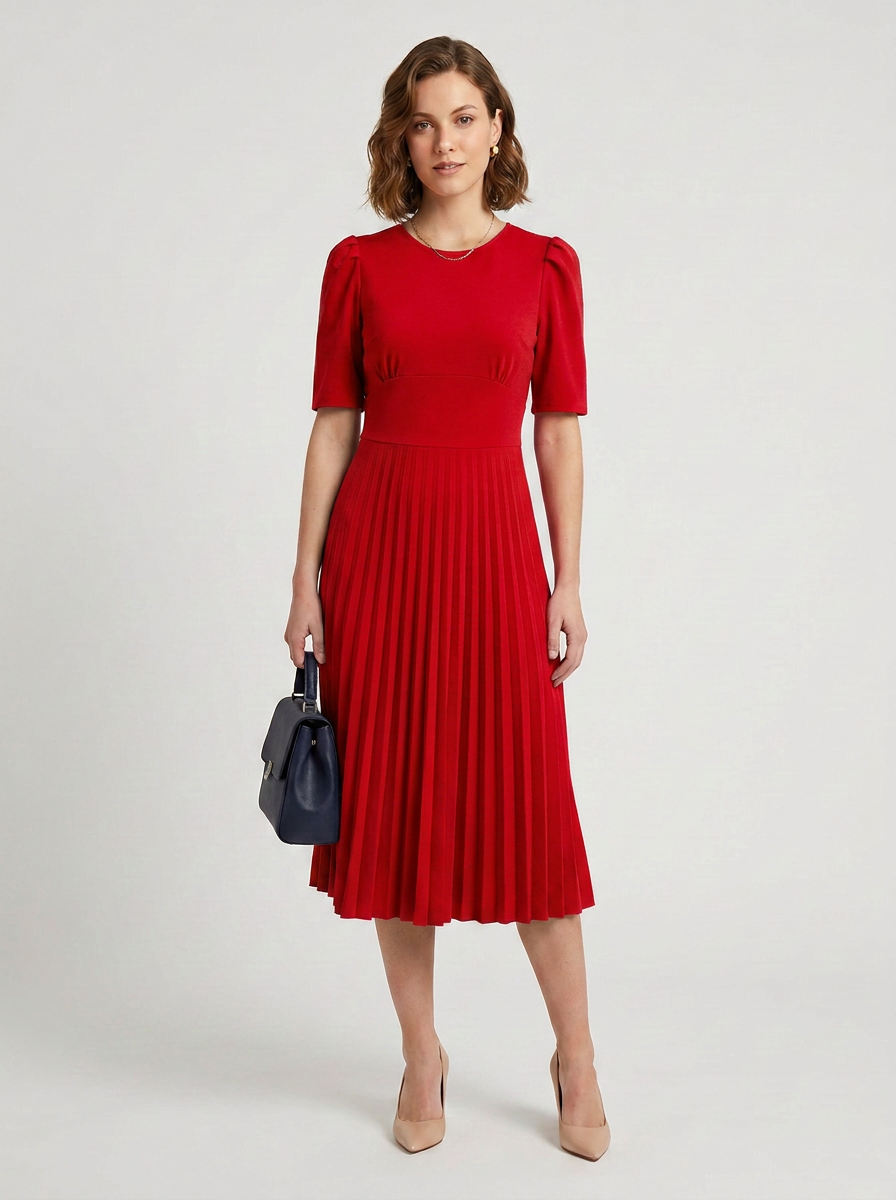 A woman modeling a bright red midi dress with short puff sleeves and a pleated skirt, holding a dark blue handbag against a light gray studio background.