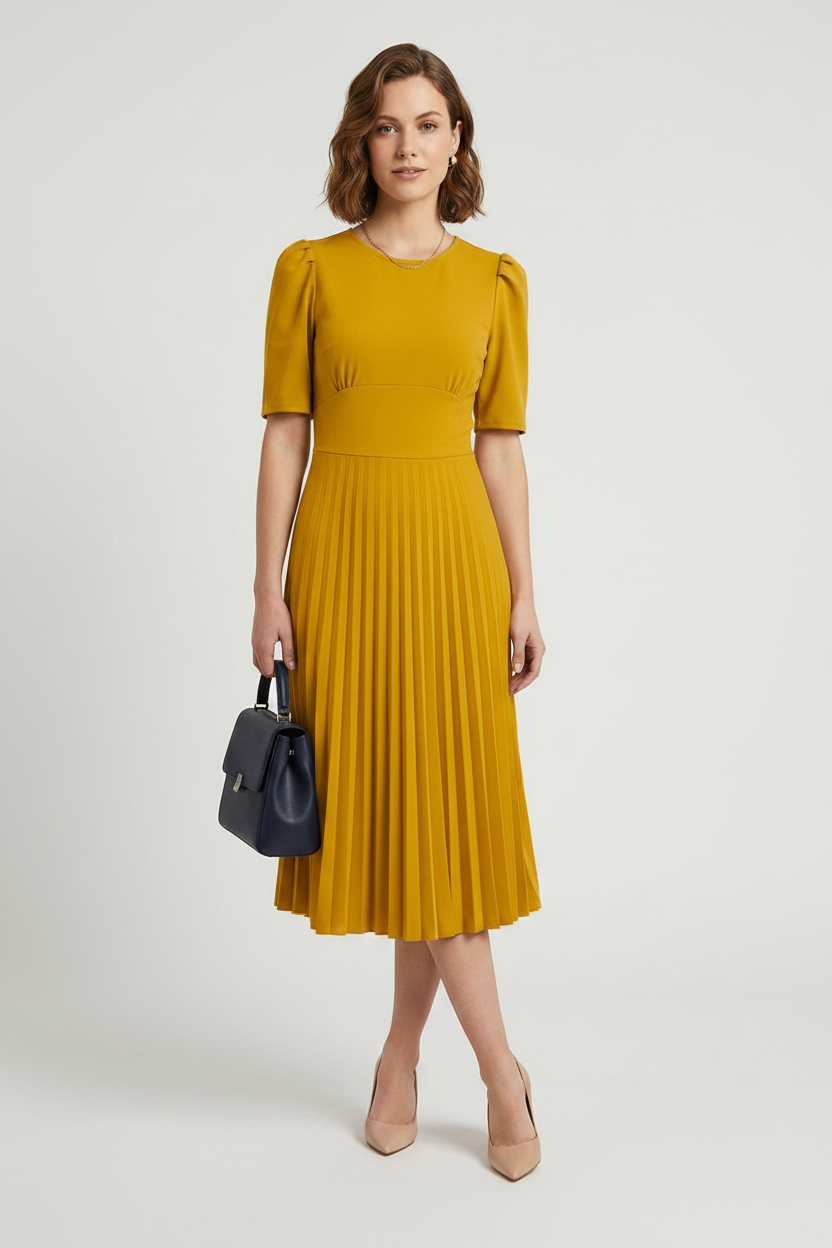 A woman modeling a mustard yellow midi dress with short puff sleeves and a pleated skirt, holding a small dark blue handbag against a light gray studio background.