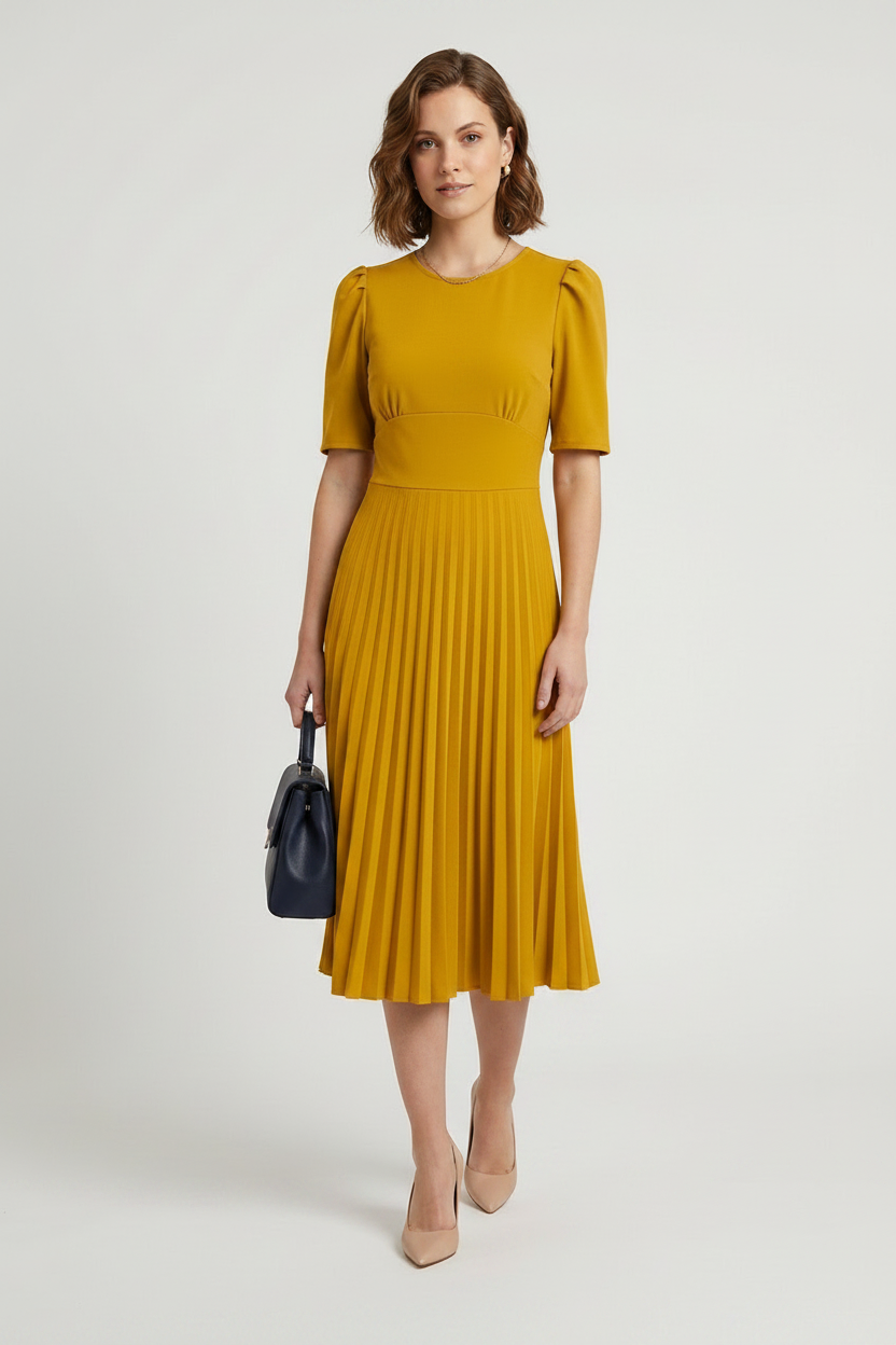 A woman modeling a mustard yellow midi dress with short puff sleeves and a pleated skirt, holding a small dark blue handbag against a light gray studio background.