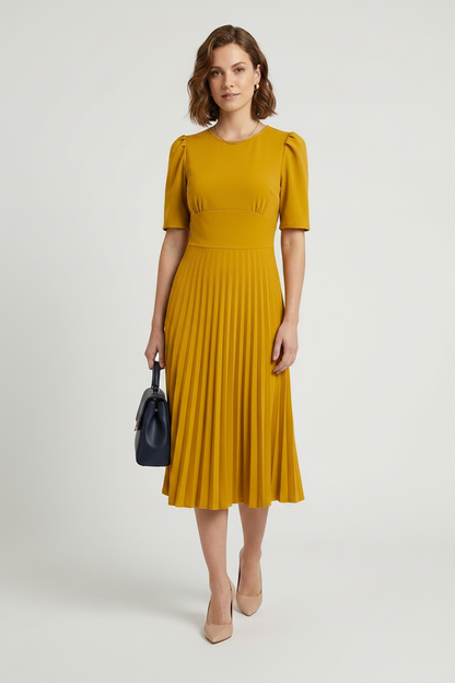 A woman modeling a mustard yellow midi dress with short puff sleeves and a pleated skirt, holding a small dark blue handbag against a light gray studio background.