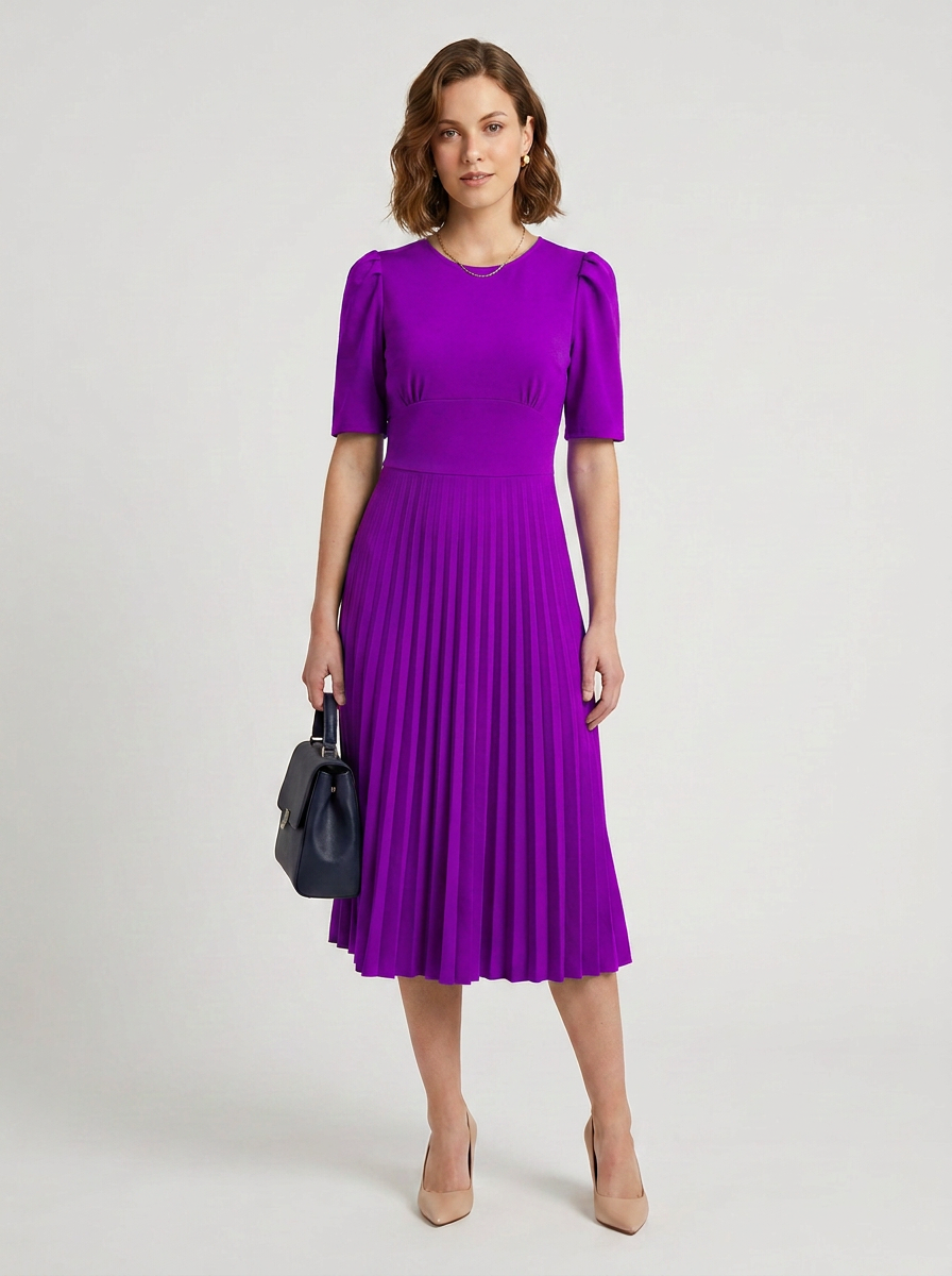 A woman modeling a bright purple midi dress with short puff sleeves and a pleated skirt, holding a small black handbag against a light gray studio background.