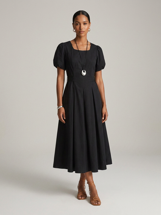 A woman modeling a black midi dress with short puff sleeves, a square neckline, and a flared skirt, photographed against a plain light gray studio background.