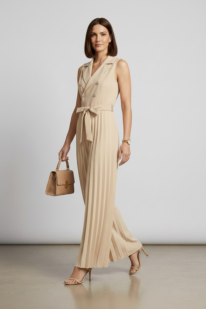 A woman models a sleeveless beige double-breasted jumpsuit with wide legs, pleated detailing, and a matching waist tie. She is holding a matching beige handbag and wearing beige high-heeled sandals against a neutral studio backdrop.