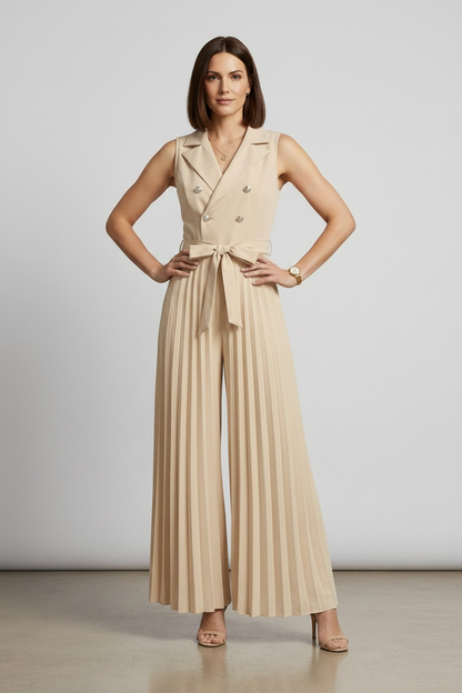 A woman models a sleeveless beige double-breasted jumpsuit with wide legs, pleated detailing, and a matching waist tie. She is holding a matching beige handbag and wearing beige high-heeled sandals against a neutral studio backdrop.