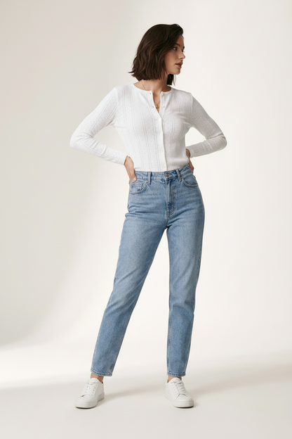 A woman modeling a white ribbed long-sleeve button-front top and light-wash blue jeans with white sneakers, standing against a plain off-white studio background.