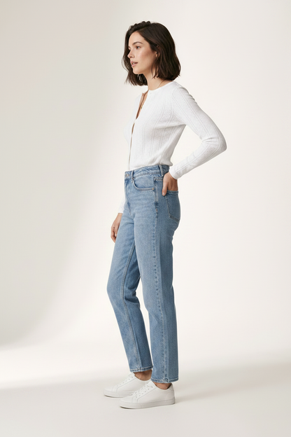 A woman modeling a white ribbed long-sleeve button-front top and light-wash blue jeans with white sneakers, standing against a plain off-white studio background.
