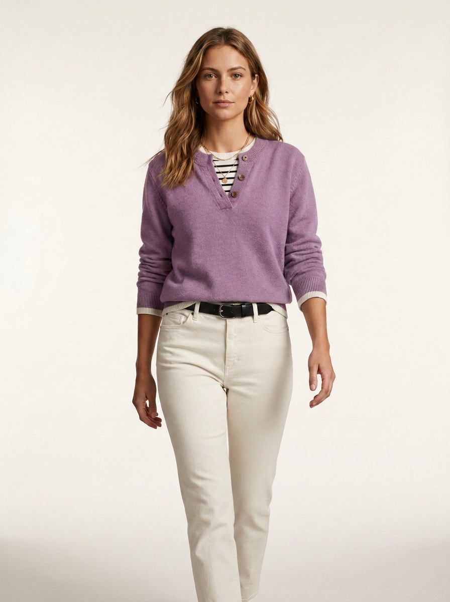 A woman modeling a lavender-purple long-sleeve knit sweater with a split neckline over a striped shirt, paired with off-white pants and a black belt, against a plain light background.