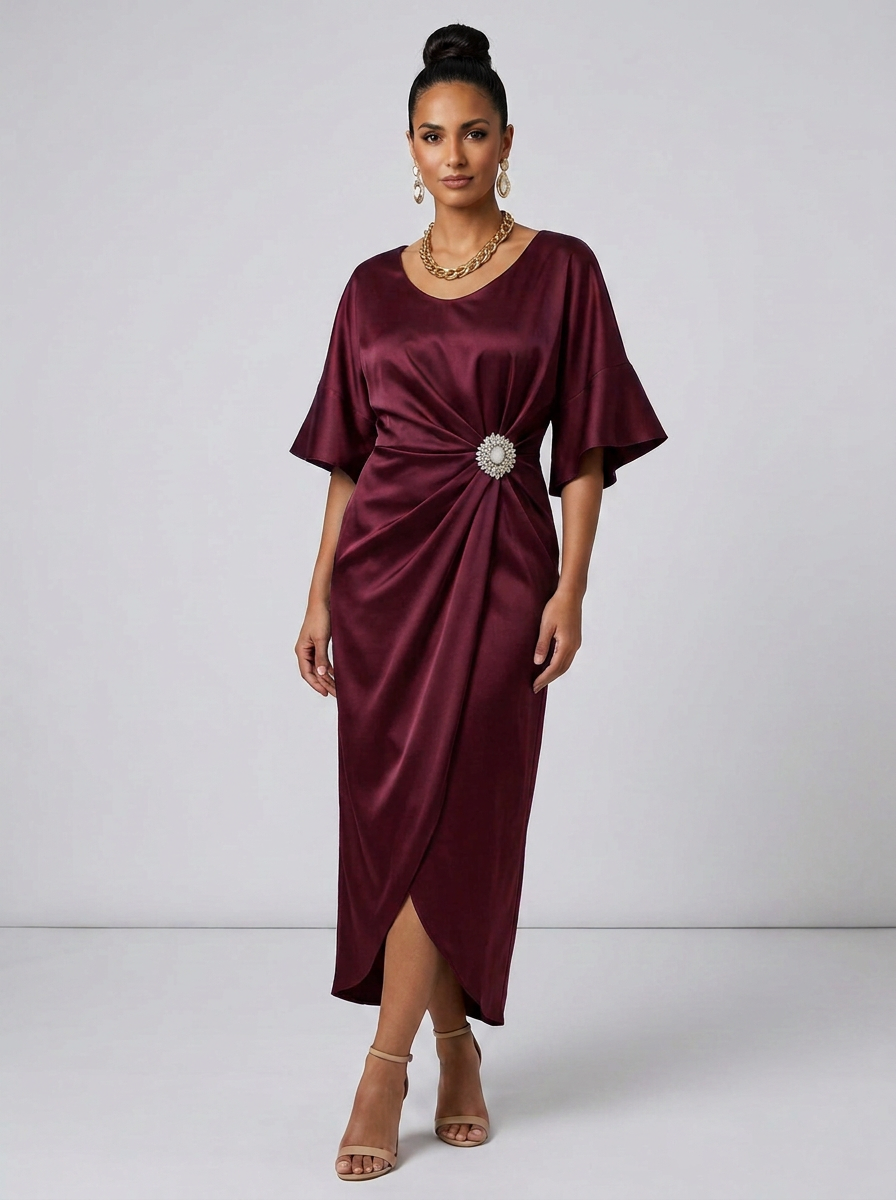 A woman models a satin-like midi dress in deep burgundy with a gathered twist detail at the waist adorned with a jeweled brooch. The dress has short flutter sleeves and a draped silhouette, paired with beige high-heeled sandals against a plain light gray studio background.