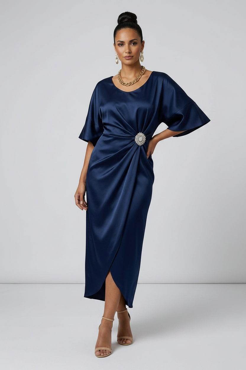 A woman models a navy blue satin midi dress with a draped, gathered design and a silver jeweled waist detail, set against a plain light gray studio background.