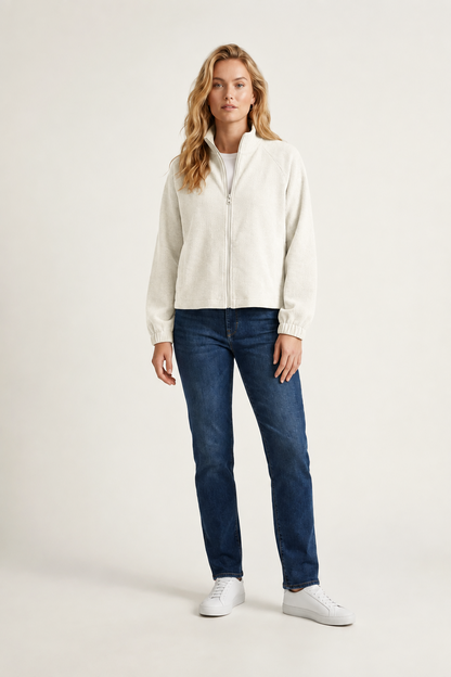 A woman modeling a light gray zip-up knit sweater, dark blue jeans, and white sneakers against a plain off-white studio background.