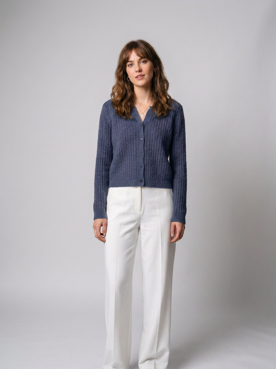A woman modeling a navy blue ribbed knit cardigan with a collar and button front, paired with white wide-leg trousers, against a neutral light gray studio background.