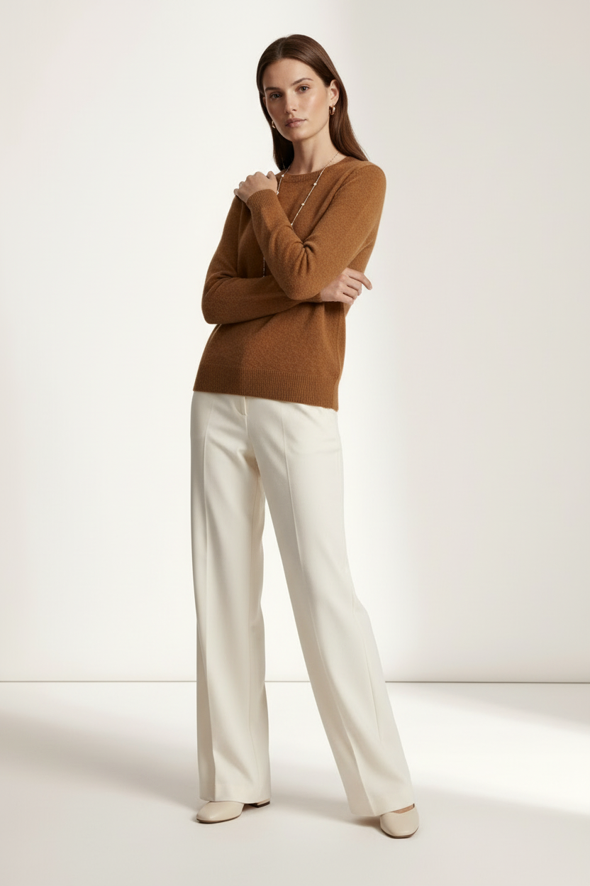 A woman modeling a warm brown knit sweater and off-white wide-leg trousers against a clean, light beige studio background.
