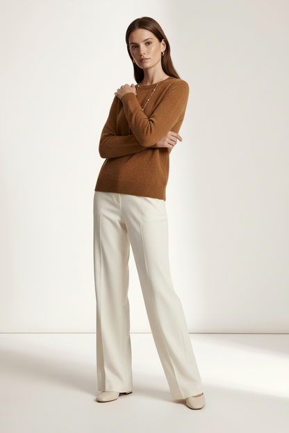 A woman modeling a warm brown knit sweater and off-white wide-leg trousers against a clean, light beige studio background.