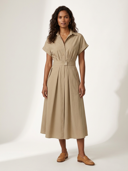 A woman modeling a beige short-sleeve midi shirt dress with a button-up front and a matching fabric tie belt at the waist, paired with tan loafers, against a plain off-white studio background.