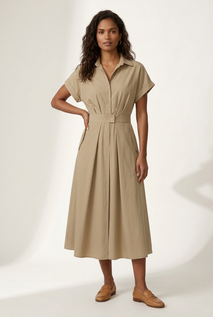 A woman modeling a beige short-sleeve midi shirt dress with a button-up front and a matching fabric tie belt at the waist, paired with tan loafers, against a plain off-white studio background.