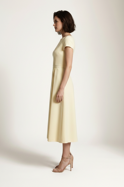 A woman modeling a pale yellow midi dress with short cap sleeves, a boat neckline, and a gathered waist, photographed against a plain light beige studio background.
