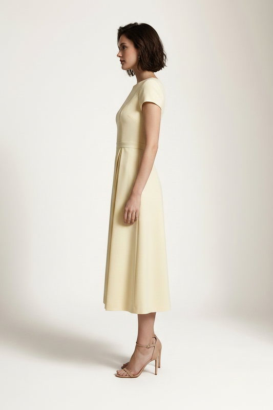 A woman modeling a pale yellow midi dress with short cap sleeves, a boat neckline, and a gathered waist, photographed against a plain light beige studio background.
