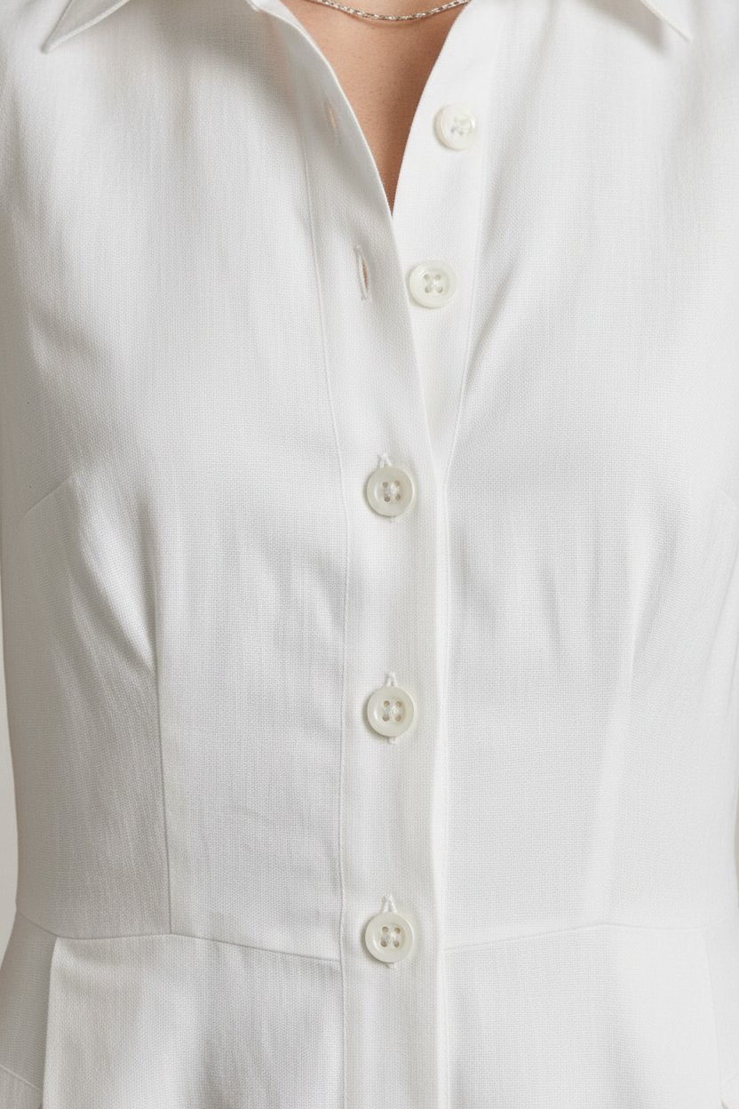A woman stands in a studio wearing a sleeveless white midi shirt dress with a button front and side pockets, paired with beige strappy sandals against a light gray background.