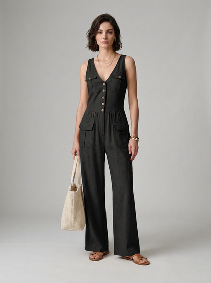 A woman models a black sleeveless wide-leg jumpsuit with gold-tone buttons down the front, holding a beige canvas tote bag against a neutral gray studio background.