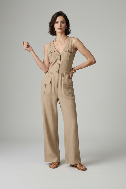 A woman models a sleeveless beige wide-leg jumpsuit with front buttons and flap pockets, holding a matching beige tote bag against a neutral gray studio background.