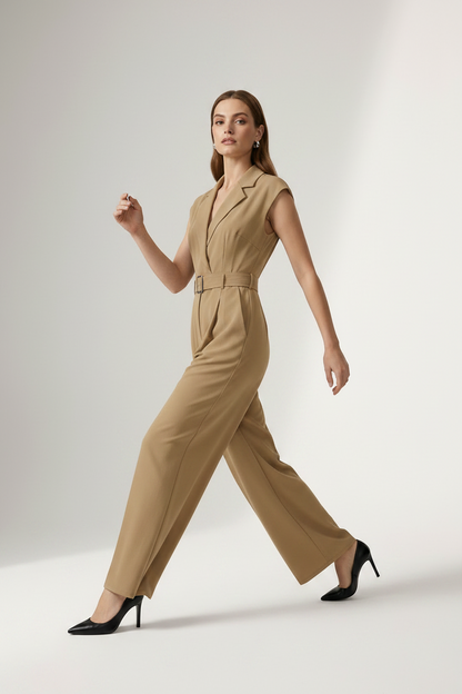 A woman modeling a sleeveless beige wide-leg jumpsuit with a matching belt and silver buckle, styled with black heels against a light gray studio background.
