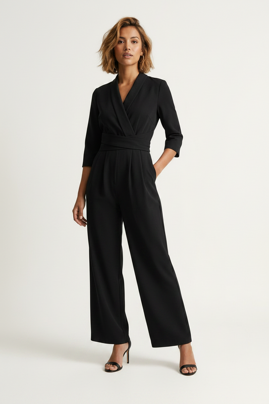 A woman modeling a black wrap-style jumpsuit with three-quarter sleeves, a self-tie waist belt, and wide legs, paired with black heeled sandals against a plain light background.