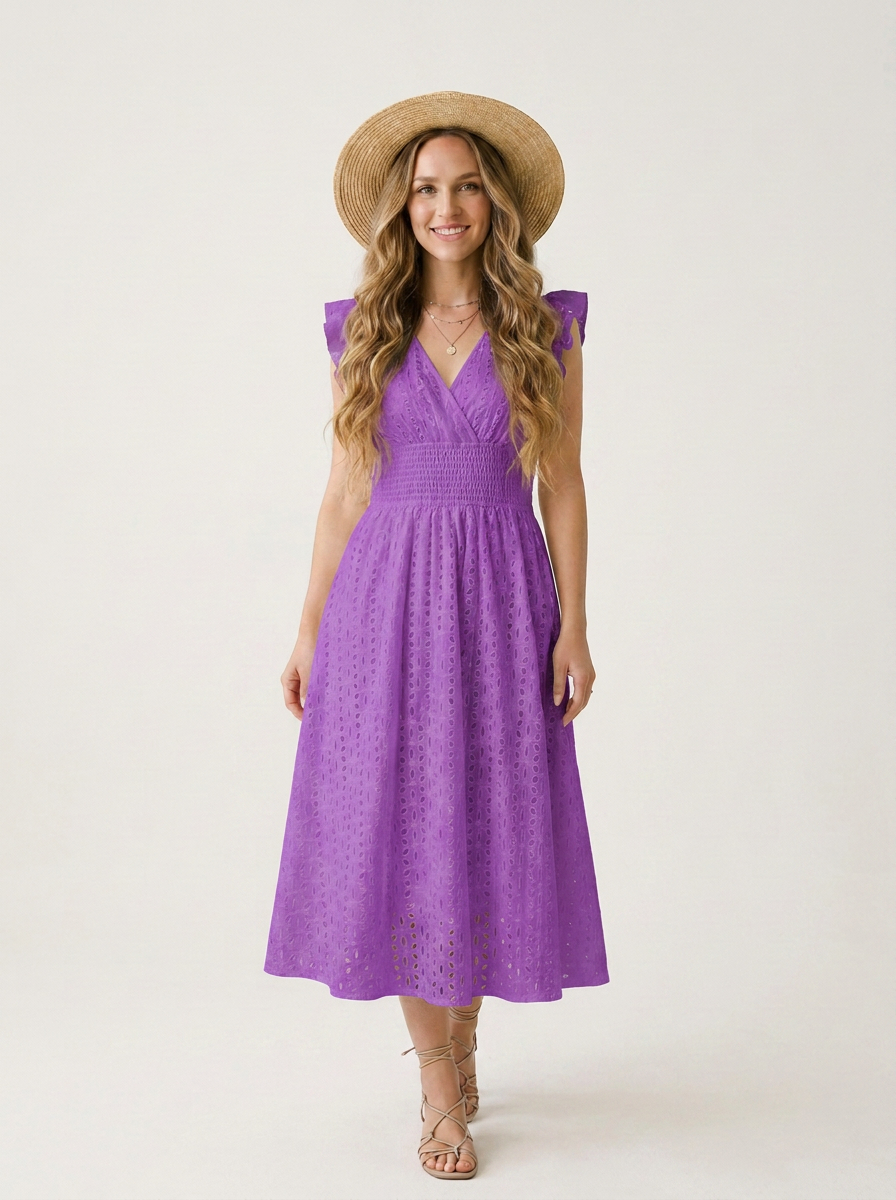 A woman modeling a purple eyelet midi dress with a V-neckline and cap sleeves, styled with a straw hat and beige strappy heels against a plain off-white studio background.