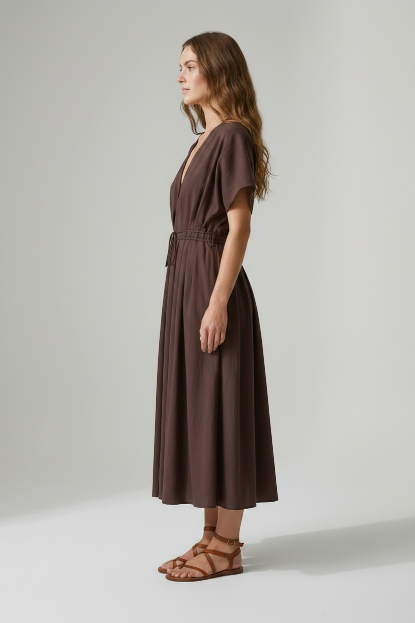 A woman modeling a dark brown midi wrap dress with short flutter sleeves, a deep V-neckline, and a drawstring waist, paired with brown strappy sandals against a neutral studio background.