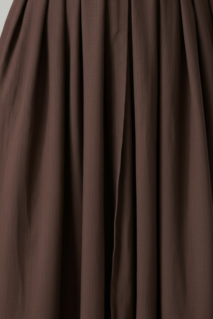 A woman modeling a dark brown midi wrap dress with short flutter sleeves, a deep V-neckline, and a drawstring waist, paired with brown strappy sandals against a neutral studio background.