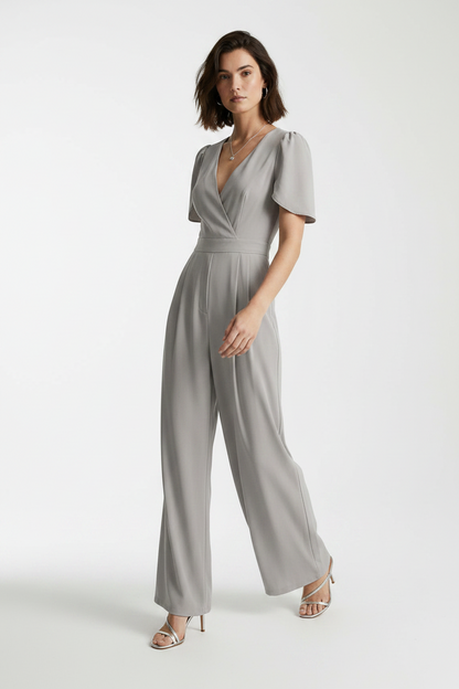 A woman modeling a light gray jumpsuit with short puff sleeves, a wrap-style V-neck bodice, and wide legs, photographed against a plain light gray studio background.
